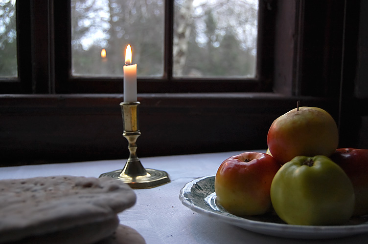 Knäckebröd, äpple och levande ljus på vit duk framför fönster