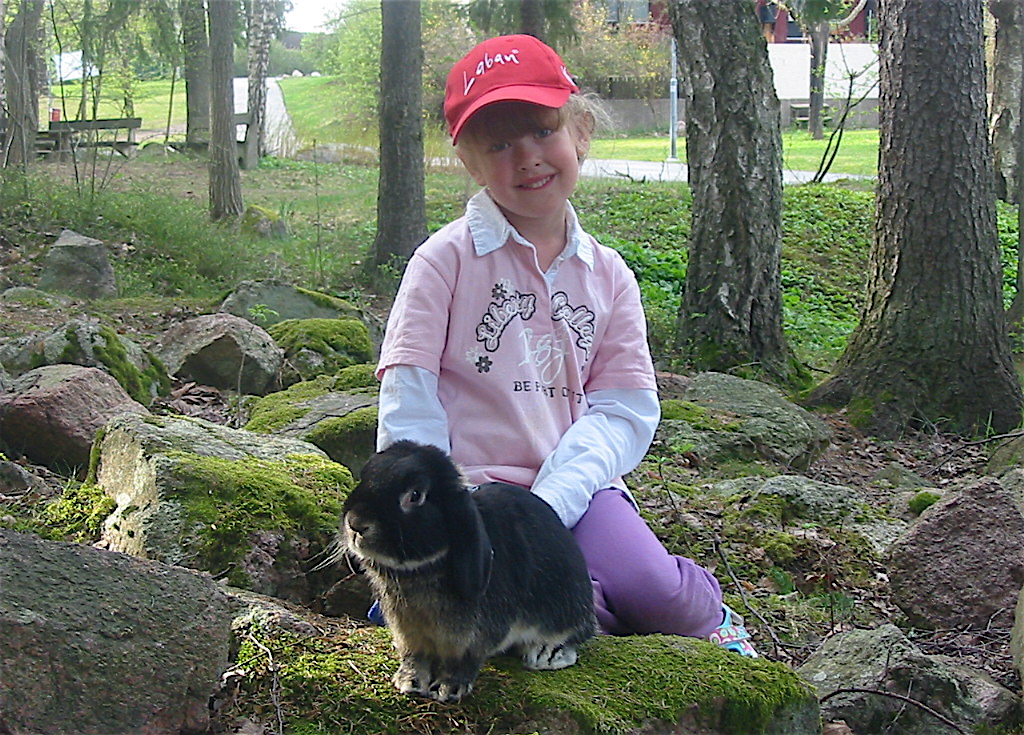 Flicka med vädurskanin i koppel bland mossiga stenar.